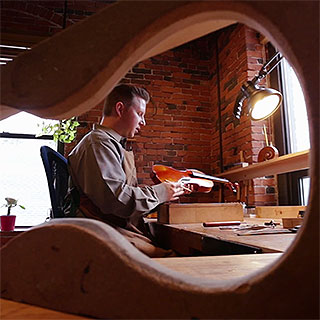 Man inspecting a violin at a workbench